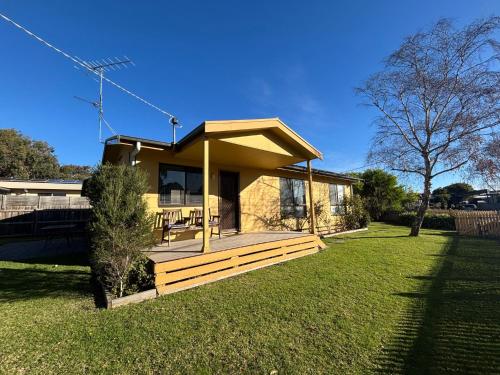 a small yellow house with a wooden deck in a yard at Alwyns By The Sea in Inverloch
