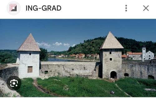 a castle with two towers and a river in the background at Camping Nori-Una in Hrvatska Kostajnica