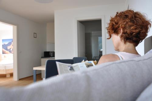 a woman sitting on a couch reading a book at Alpenchalet Apartments in Parcines