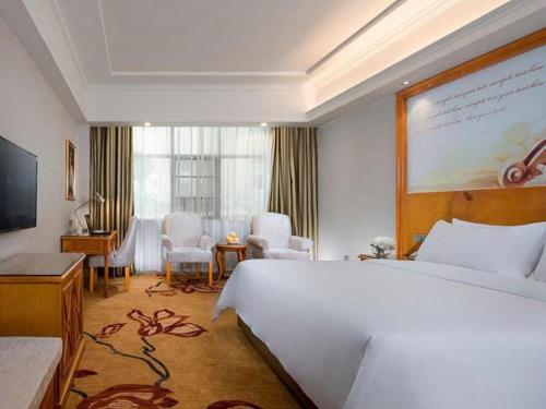 ein Hotelzimmer mit einem großen weißen Bett und einem Schreibtisch in der Unterkunft Vienna Hotel Hunan Shaoyang South Railway Station in Shaoyang