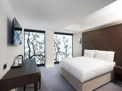 1 dormitorio con cama blanca, escritorio y ventanas en Central Park Hotel, en Londres