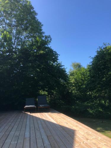 two benches sitting on a wooden deck with trees at Liseleje sommerhus på naturgrund in Melby