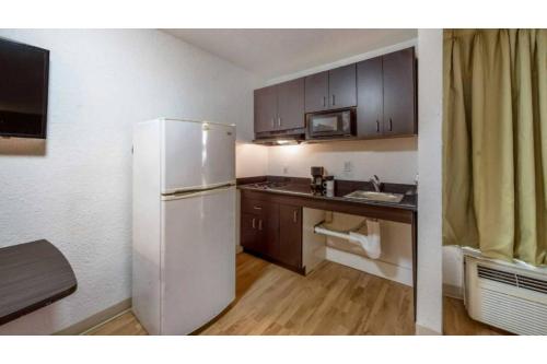a kitchen with a white refrigerator and wooden cabinets at Studio 6 Irving, TX - Irving DFW Airport East in Irving