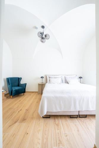 a white bedroom with a bed and a blue chair at Zámek Načeradec in Načeradec