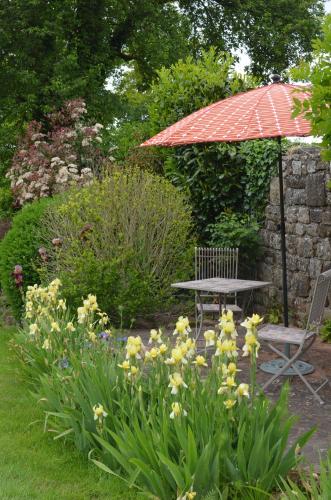 a table and an umbrella in a garden with flowers at The Farmhouse La Drutière in Saint-Sauveur-de-Carrouges