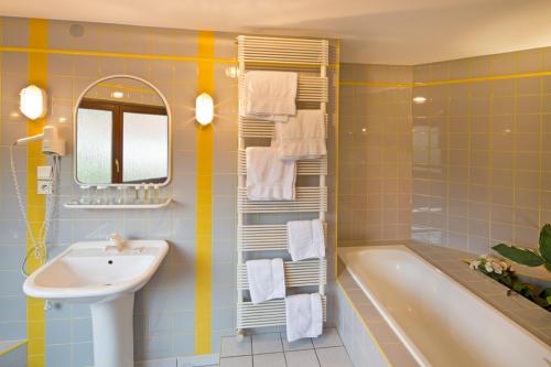 La salle de bains est pourvue d'un lavabo, d'une baignoire et d'un miroir. dans l'établissement Hotel Au Vieux Moulin, à Graufthal