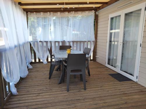 Una mesa de comedor y sillas en un porche con cortinas. en Mobil home le Sunny, en Lège-Cap-Ferret