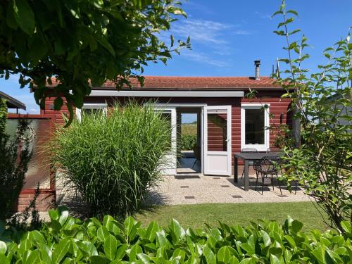 a red house with a white door and a patio at Kings View Cottage, nu met nieuwe grote BBQ in Warmenhuizen