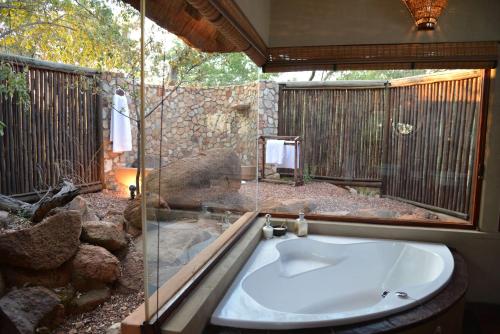 a bathroom with a bath tub with a glass window at Thakadu Bush Lodge Naka Sanga in Mabula