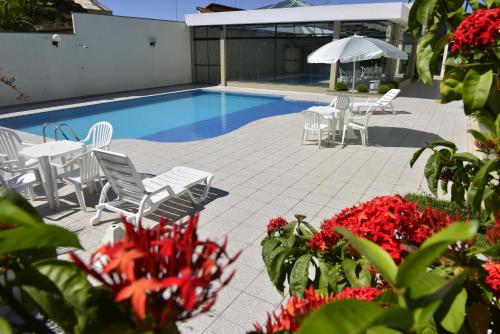 a swimming pool with white chairs and tables and red flowers at Biazi Plaza Hotel in Bauru