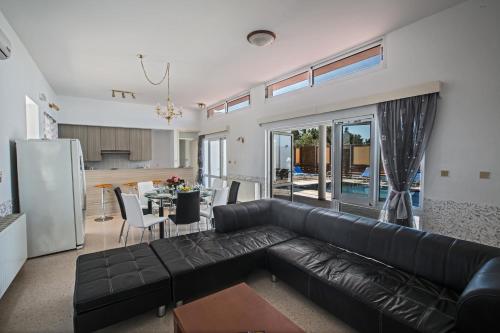 a living room with a black leather couch and a kitchen at Napa Nissi House in Ayia Napa