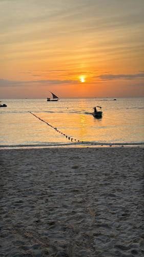 a boat in the water at sunset on the beach at Villa Peace And Color in Nungwi