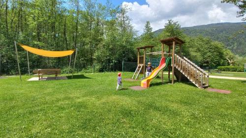 a child standing in the grass next to a playground at VERONIKA Haus KMB Seeappartement am Ossiacher See mit direktem Seezugang und Hallenbad in Tschöran