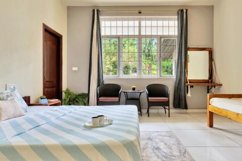 a bedroom with a bed and chairs and a window at SaffronStays Robin Woods in Kenchamman Hoskota