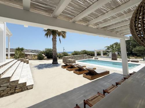 a patio with a pool and chairs and a palm tree at CASA GEKKO - MYKONOS by ROOMERS HOTELS in Mýkonos City