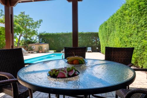 a table with a bowl of fruit on it next to a pool at Villa Aspasia in Peyia, Private Pool & 3 Ensuite Bedrooms in Paphos