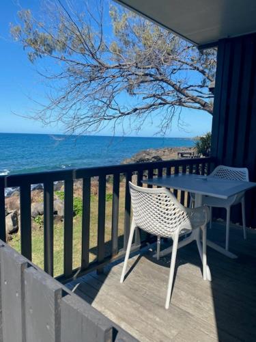 a table and a chair on a balcony with the ocean at Absolute Oceanfront Tourist Park in Bargara