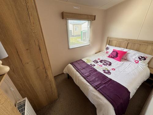 ein Schlafzimmer mit einem Bett mit rosa Kissen und einem Fenster in der Unterkunft Palm Grove 118 - Golden Palm Resort - pet friendly, Wi-Fic close to the beach - Meadow Lakes Caravan & Lodge Hire in Chapel Saint Leonards