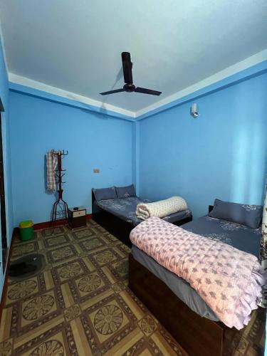 a blue room with two beds and a ceiling fan at Hotel Atithi Devo Bhava in Lālbhitti