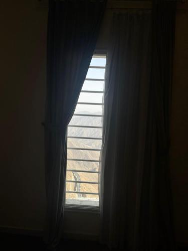 a window with a blue curtain with a view at الابنوس للشقق الفندقية in Abha