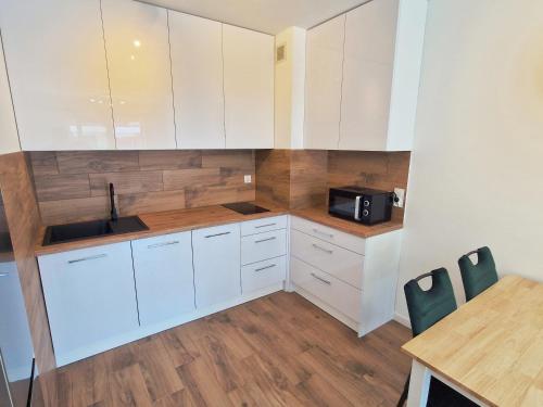 eine Küche mit weißen Schränken, einem Tisch und einer Mikrowelle in der Unterkunft Apartamenty Złote Wydmy - Plażowa Park Międzywodzie in Międzywodzie