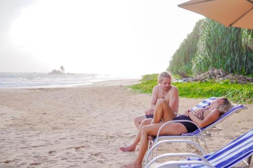 two people are sitting on the beach at Exotica Bungalows in Hikkaduwa