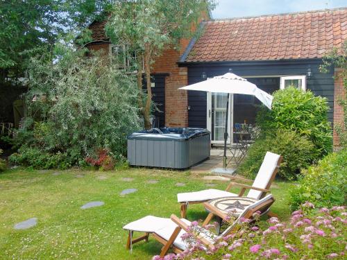 a garden with an umbrella and chairs and a hot tub at The Coach House - Ukc2365 in Watton