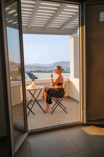 a woman sitting in a chair on a balcony at The Noverian Bios Caldera Sunset Suites in Akrotiri