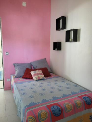 a bed in a room with a pink wall at La maison bleue pieds dans l'eau in Petite Verger