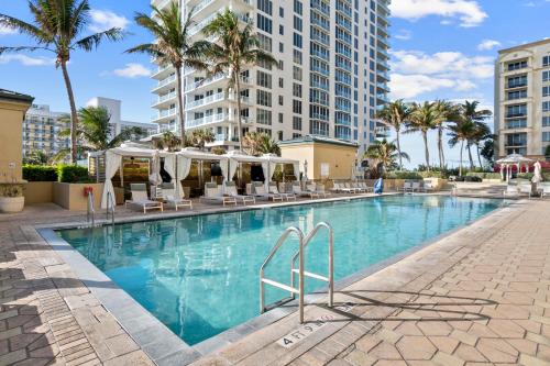 a swimming pool with chairs and palm trees and buildings at Oceanfront Palm Beach Resort & Spa Singer Island in Riviera Beach