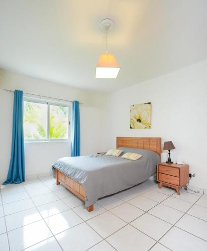 a bedroom with a bed and a window with blue curtains at Your west coast getaway in Flic-en-Flac