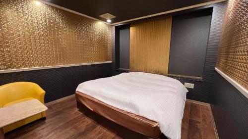 a small room with a bed and a yellow chair at ホテルリンクス in Kashiwa
