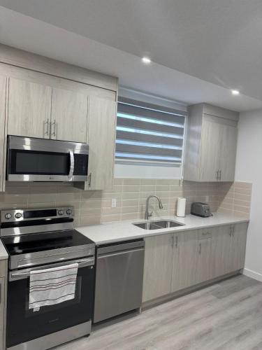 a kitchen with a stove and a sink and a microwave at Cozy Inn new basemt wt sep entrance contains 1 bdrm and den for up to 4 guests in Airdrie