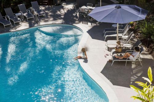 a swimming pool with chairs and an umbrella and people sitting around it at Noosa International Resort in Noosa Heads