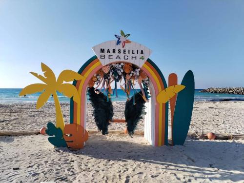 a sign on a beach with a surfboard on the beach at قرية مارسيليا بيتش فور in Sīdī ‘Abd ar Raḩmān