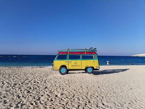 a yellow van with a surfboard on the beach at قرية مارسيليا بيتش فور in Sīdī ‘Abd ar Raḩmān