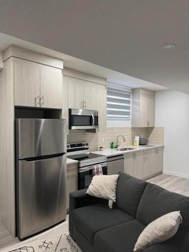 a kitchen with a couch and a stainless steel refrigerator at Cozy Inn new basemt wt sep entrance contains 1 bdrm and den for up to 4 guests in Airdrie