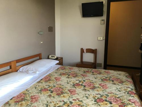 a bedroom with a bed with a floral bedspread and a chair at Hotel Plutone in Cervia