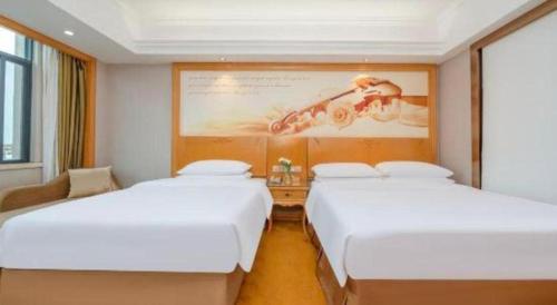 two beds in a hotel room with a picture on the wall at Vienna Hotel Guangxi Fangcheng in Fangcheng
