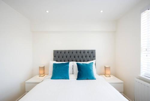 a white bedroom with a large bed with blue pillows at Romford - Balcony - Outdoor Space - Parking Space in Romford