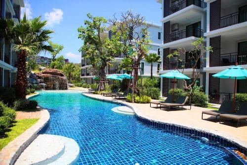 una piscina en un hotel con sillas y sombrillas en C130 Steps to Beach 1BR Condo Gym, Pool & Sauna, en Rawai Beach