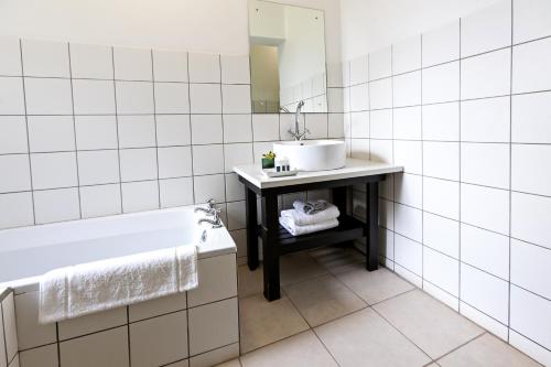 a white tiled bathroom with a sink and a tub at Leipzig Country House & Winery in Nuy