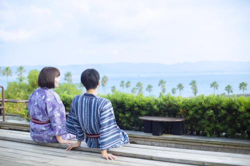 a couple of people sitting on a bench looking at the ocean at Ooedo Onsen Monogatari Hotel Ranpu in Hirado