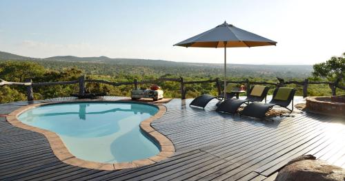 a swimming pool on a wooden deck with chairs and an umbrella at Thakadu Bush Lodge Naka Sanga in Mabula