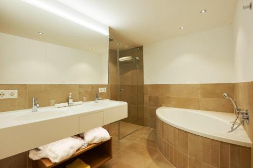a bathroom with a sink and a tub and a mirror at Après Post Hotel in Stuben am Arlberg