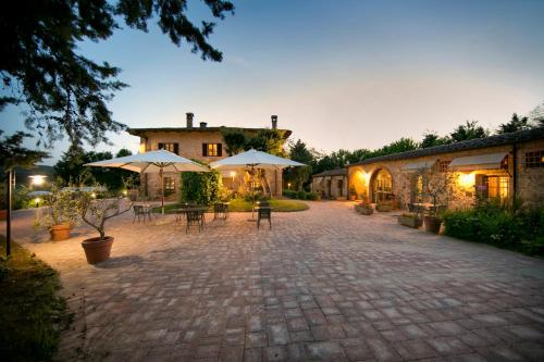 a courtyard with tables and umbrellas in front of a building at IL COLOMBAIO WINERY & Rooms in Monteriggioni