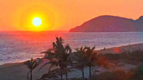 a sunset over a beach with palm trees and the ocean at Villa Star of the Sea in Barra de Navidad