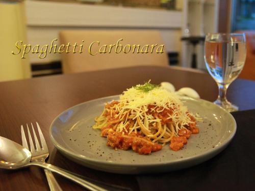 a plate of pasta on a table with a fork and a glass at Soeltan Luxe Hotel Lampung in Bandar Lampung