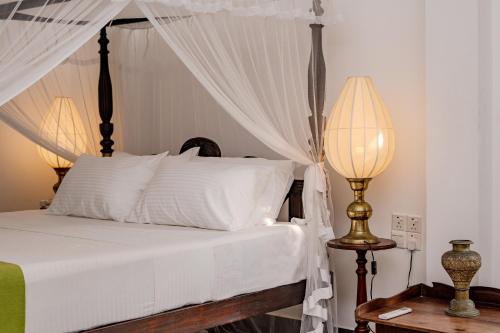 a bedroom with a bed with white sheets and two lamps at Wasantha Garden Hotel Restaurant & Ayurvedic Treatment in Weligama
