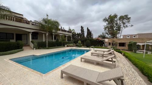 a swimming pool with two benches and a house at Gite jnanefes in El Jadida